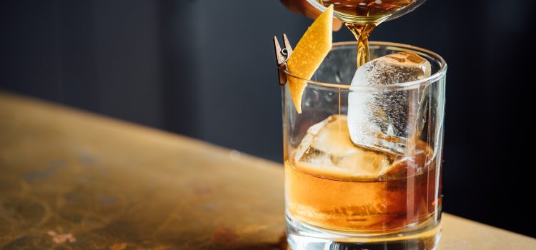 Rare Whisky being poured out of Boston shaker into glass with ice and orange peel