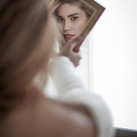 Woman looking in mirror considering Non-Surgical Nose Reshaping