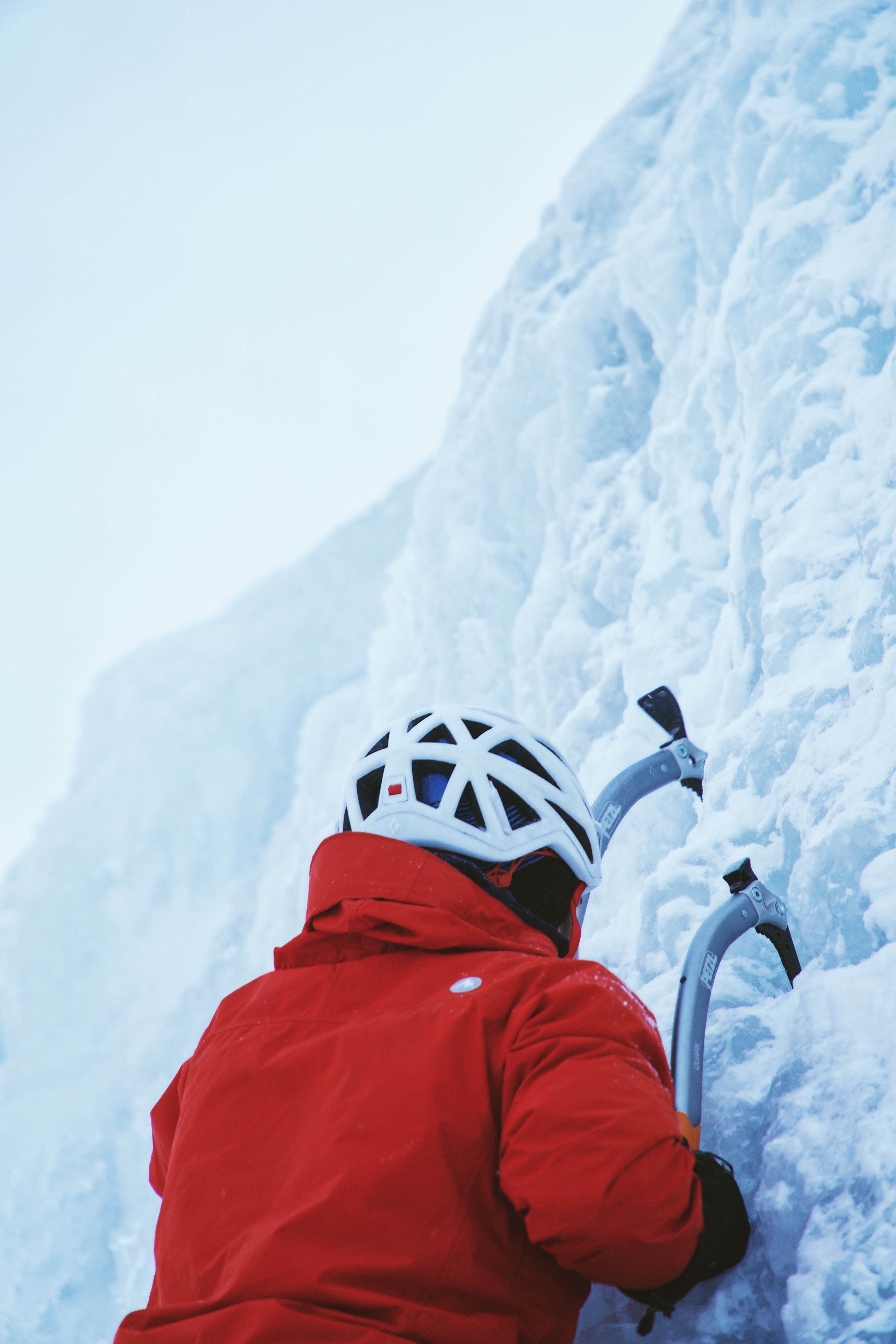 Person using ice pics to climb up the side of a snowy mountain